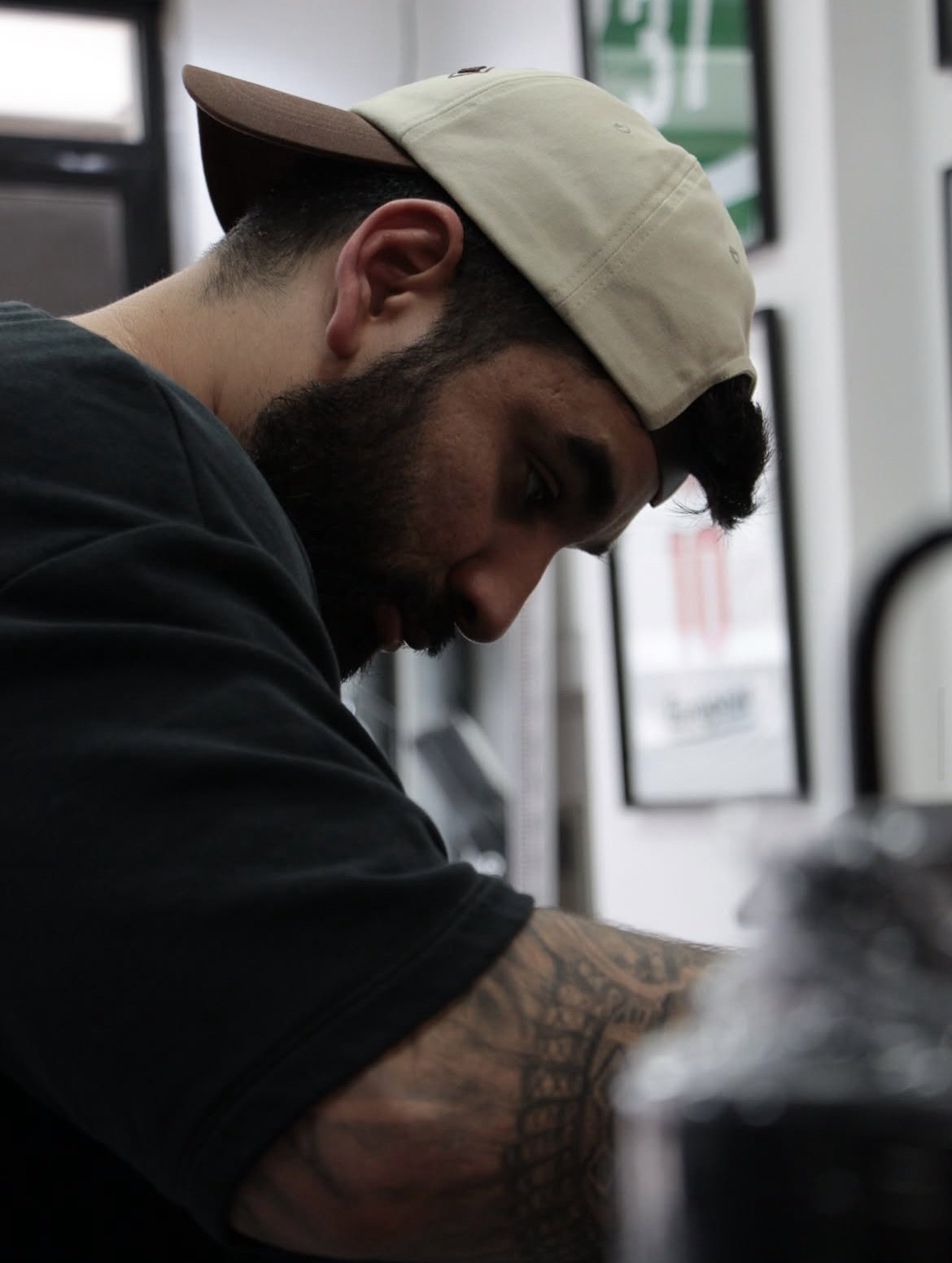 Daniel Muniz concentrado a tatuar, de boné